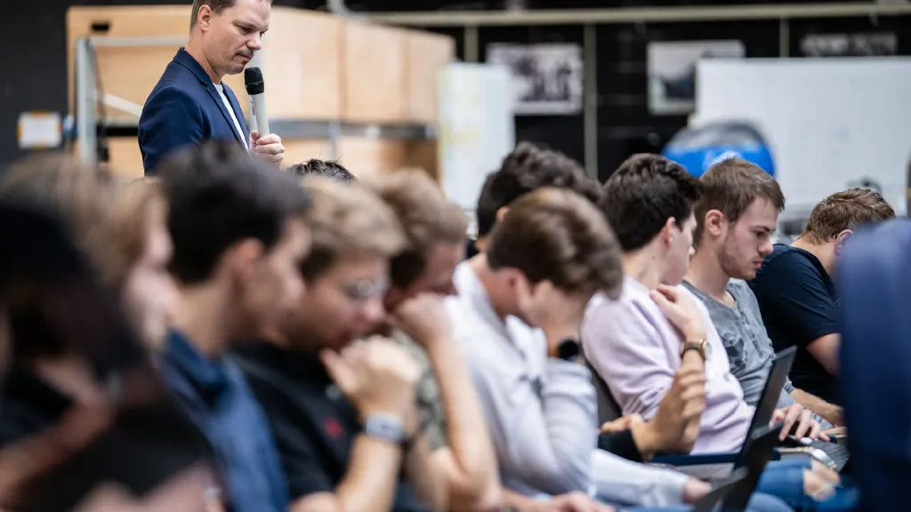 Maurice spreekt met microfoon tegen nadenkende studenten