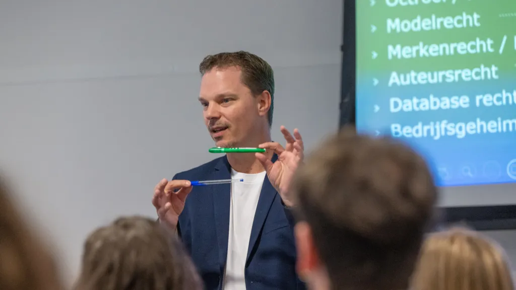 Maurice laat 2 verschillende pennen zien aan studenten. In achtergrond een scherm met verschillende IE-rechten