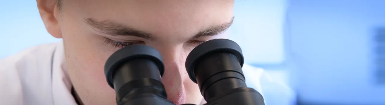 Close up van persoon in labjas die door microscoop kijkt