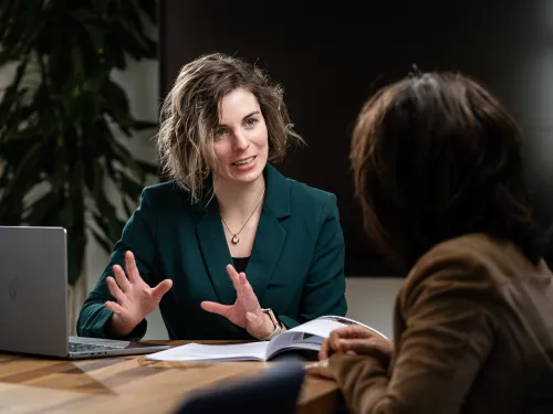 Adviseur legt iets uit aan klant. Op tafel een laptop en een document