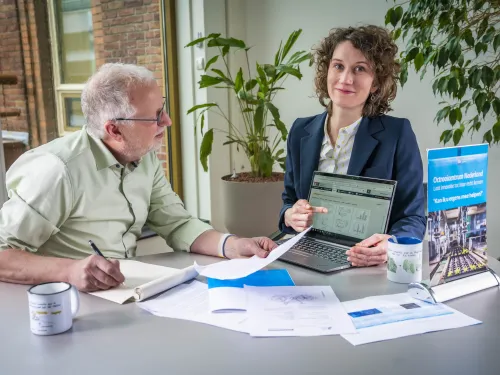 Adviseur wijst naar computerscherm. Klant kijkt waar zij naar wijst en schrijft op notitieblok