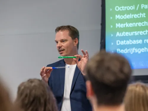 Maurice laat 2 verschillende pennen zien aan studenten. In achtergrond een scherm met verschillende IE-rechten