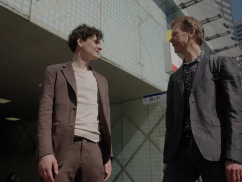 2 mannen in pak staan buiten voor een gebouw en zijn in gesprek