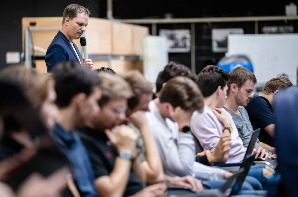 Maurice spreekt met microfoon tegen nadenkende studenten